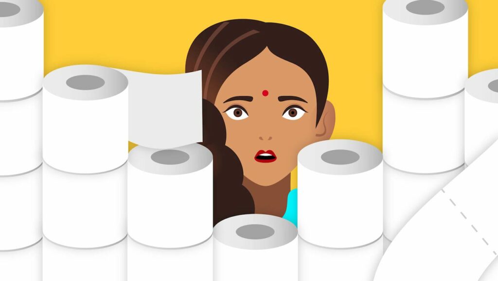 Laxmi staring behind a bunch of toilet paper rolls looking shocked